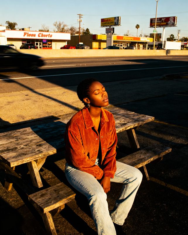 a woman sitting on a wooden bench in front of a gas station