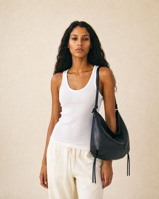 a woman in a white tank top holding a black purse
