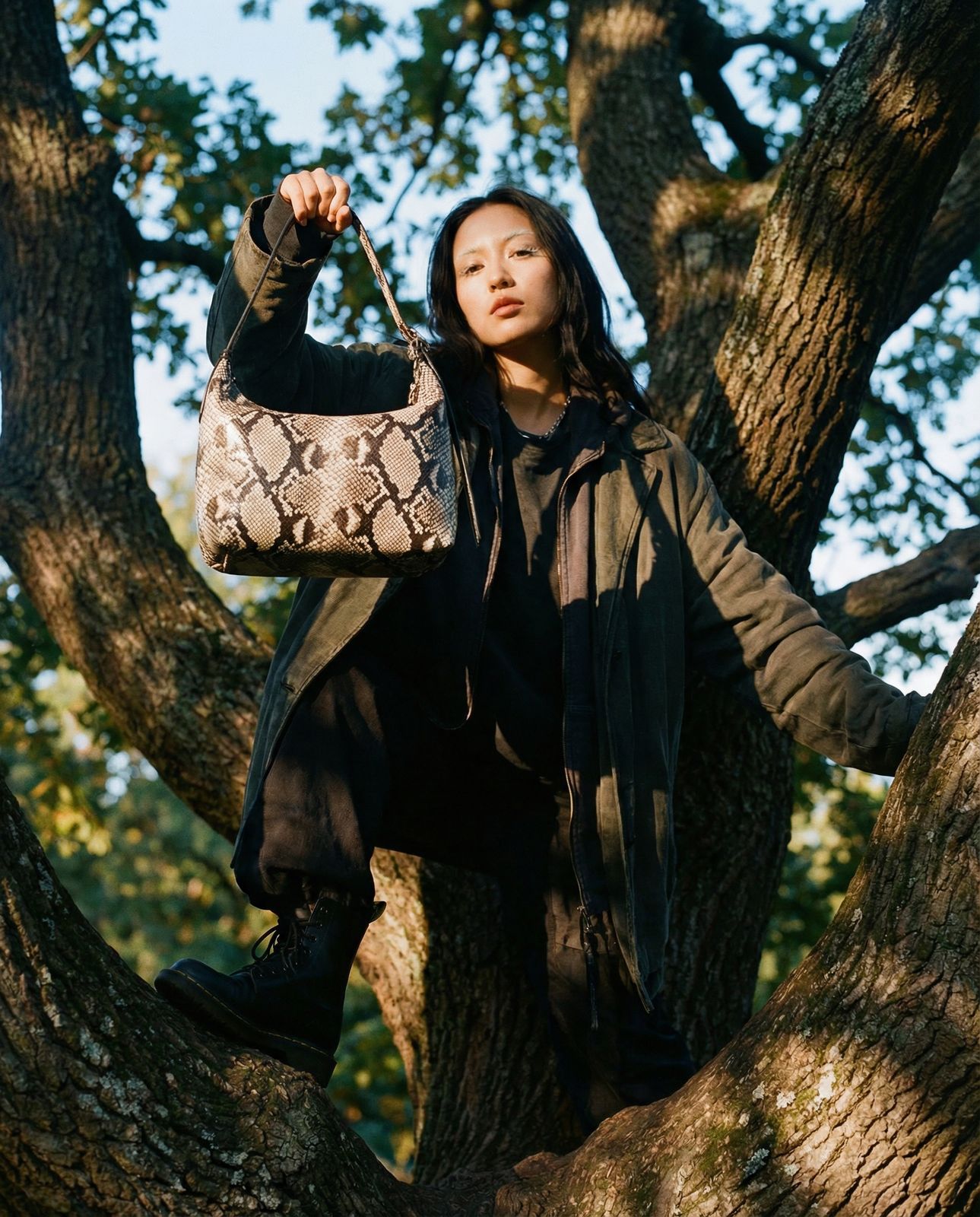 a woman sitting in a tree holding a snake skin purse