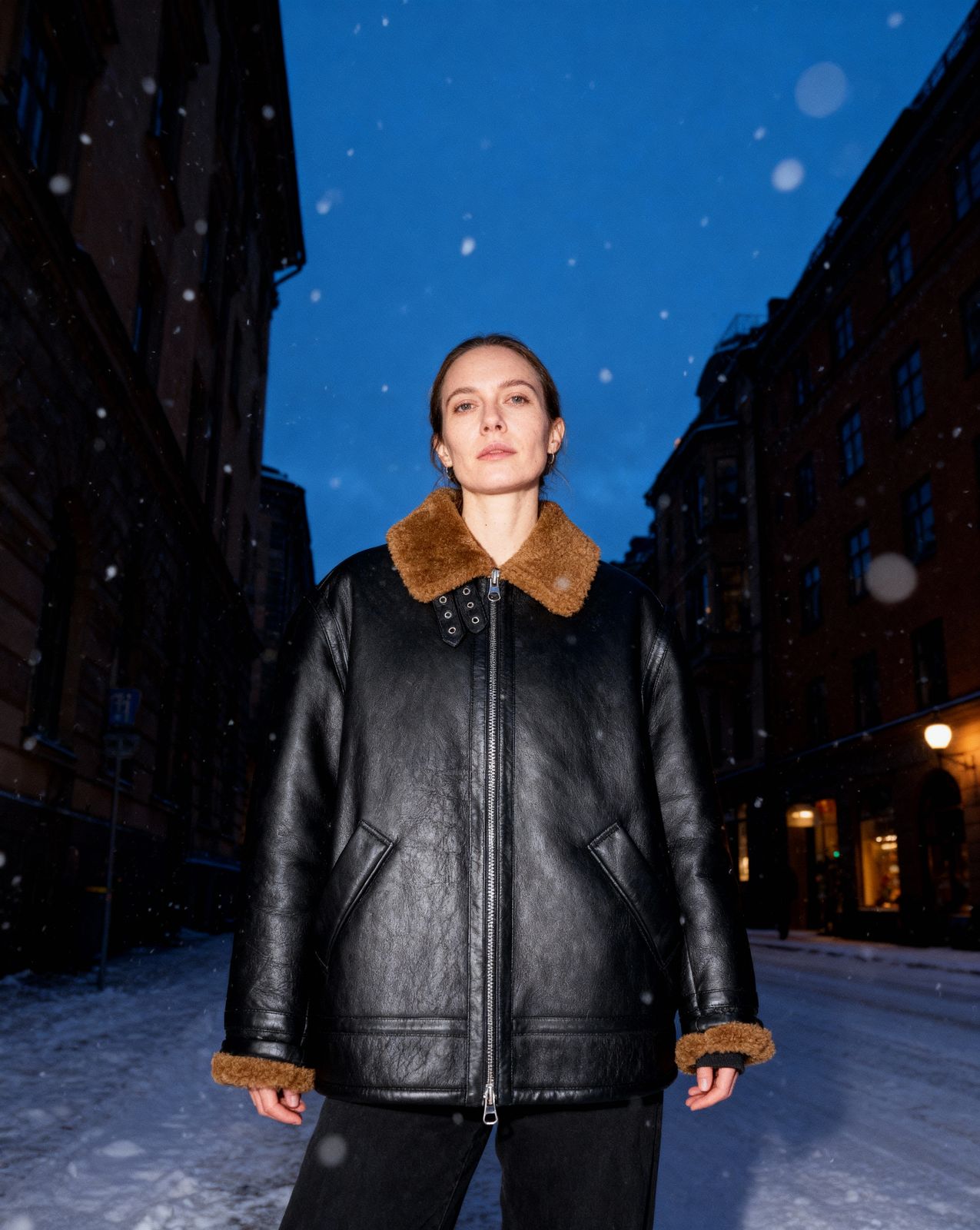 a woman standing in the snow wearing a black leather jacket