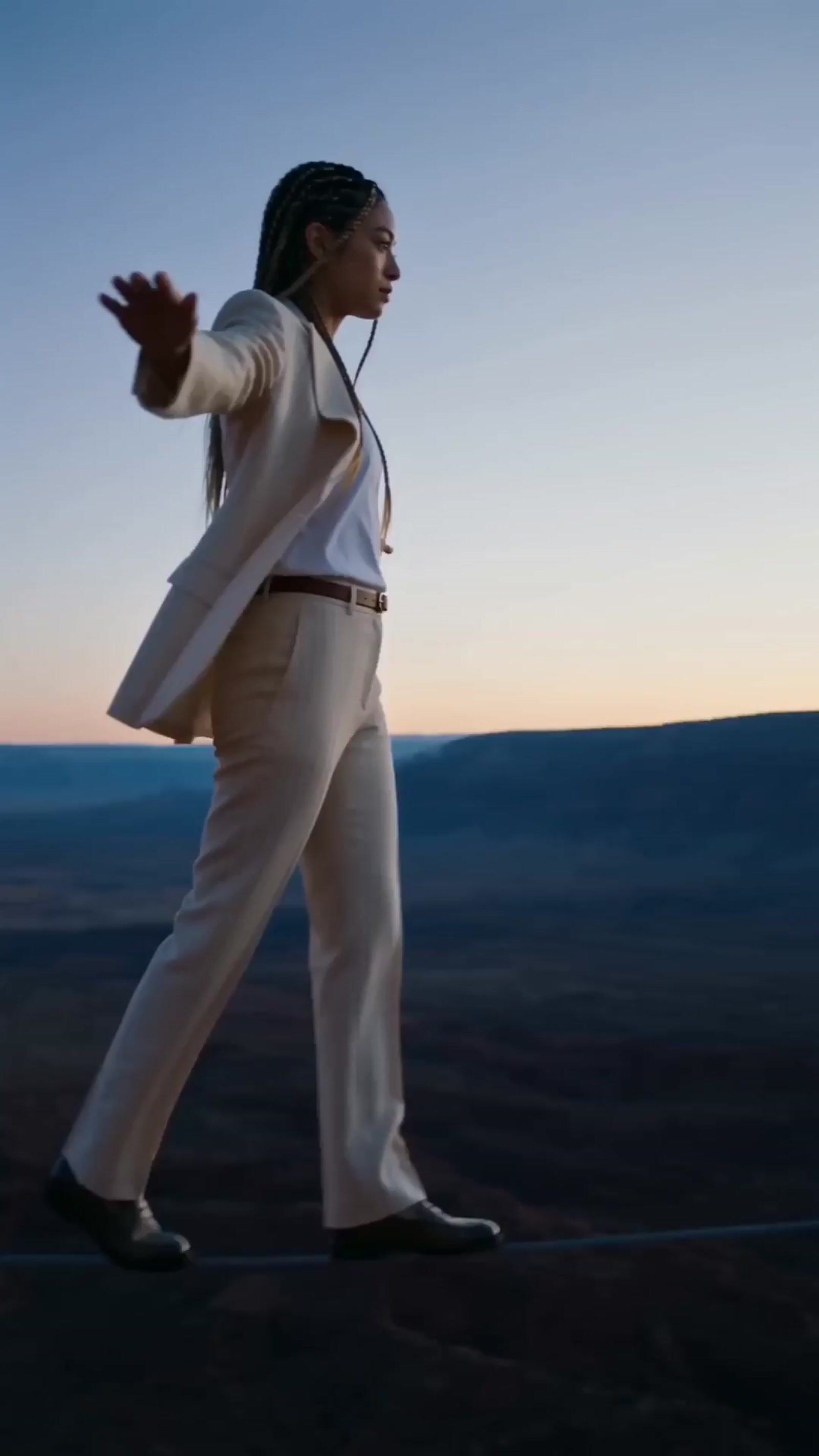 a woman in a white suit walking across a desert