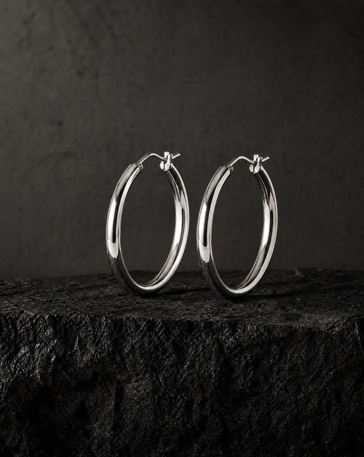 a pair of silver hoop earrings sitting on top of a rock