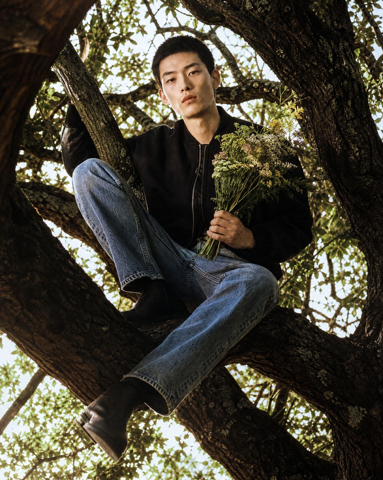 a man sitting in a tree holding a bunch of flowers