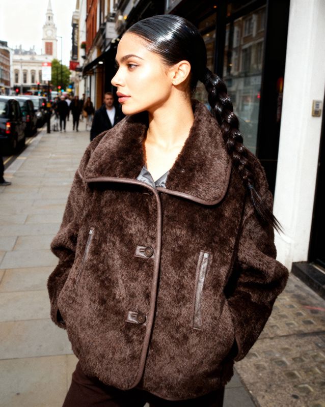 a woman is walking down the street in a brown coat