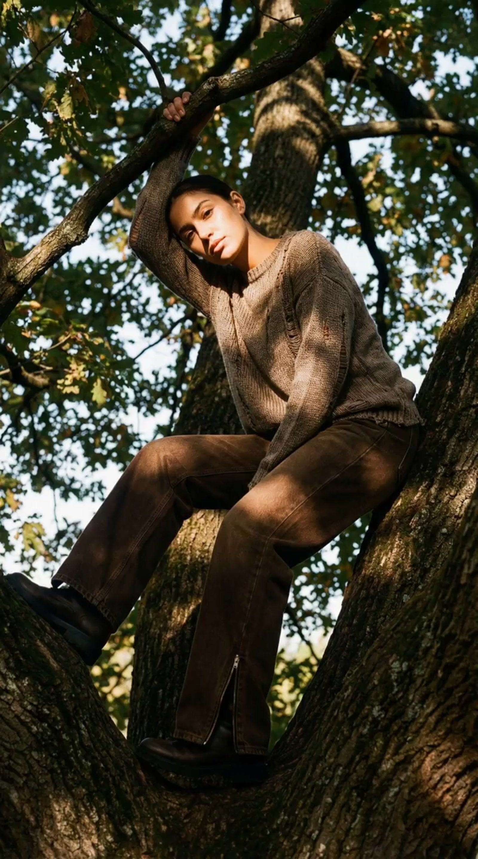 a young man sitting in a tree with his hands on his head