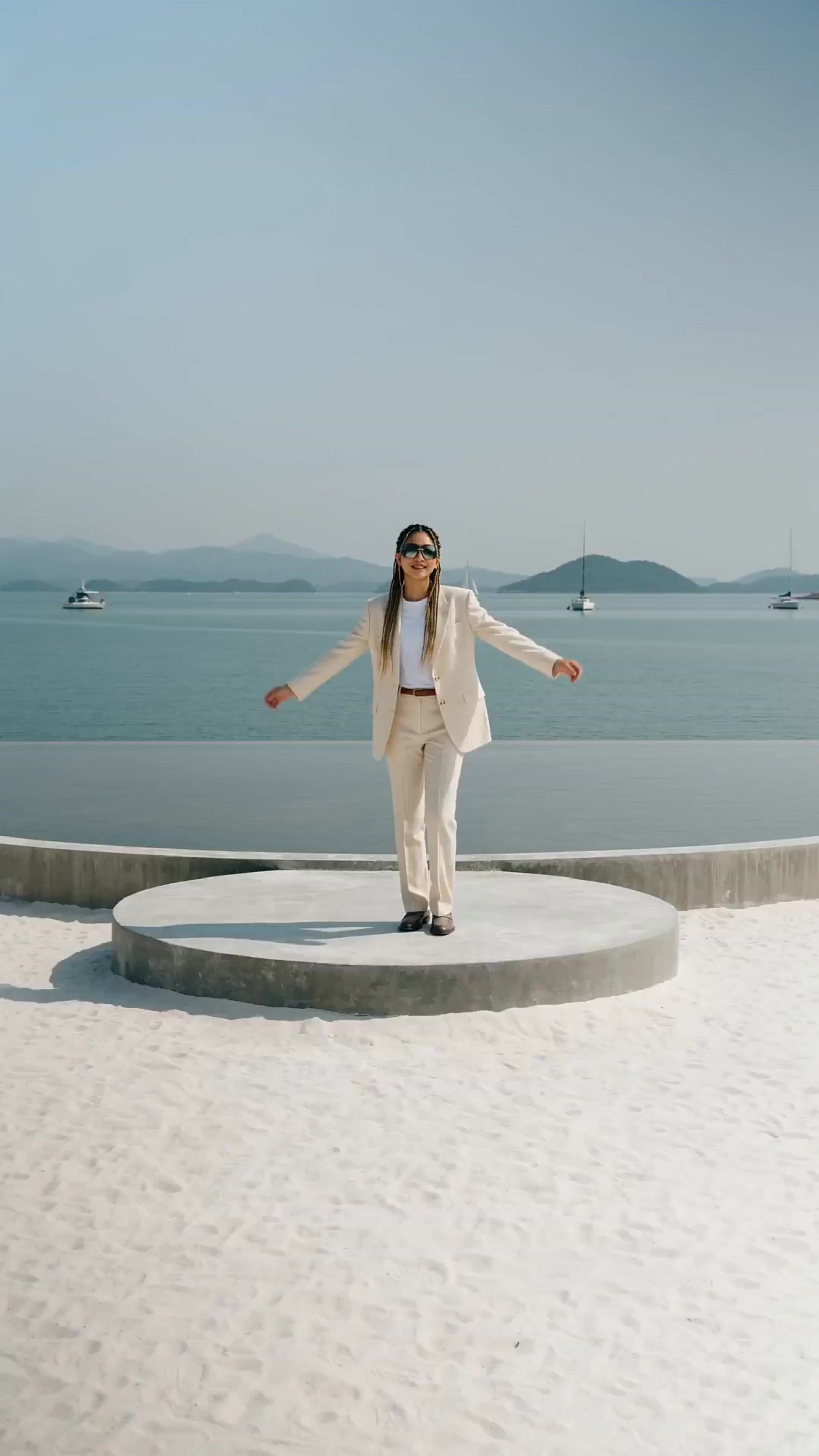 a woman in a white suit and sunglasses standing on a concrete platform