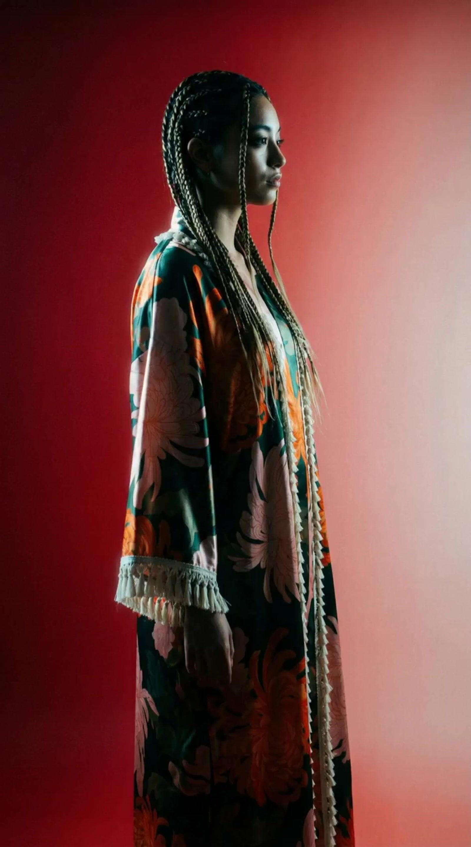 a woman with braids standing in front of a red background