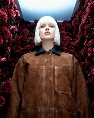 a woman standing in front of a wall of flowers