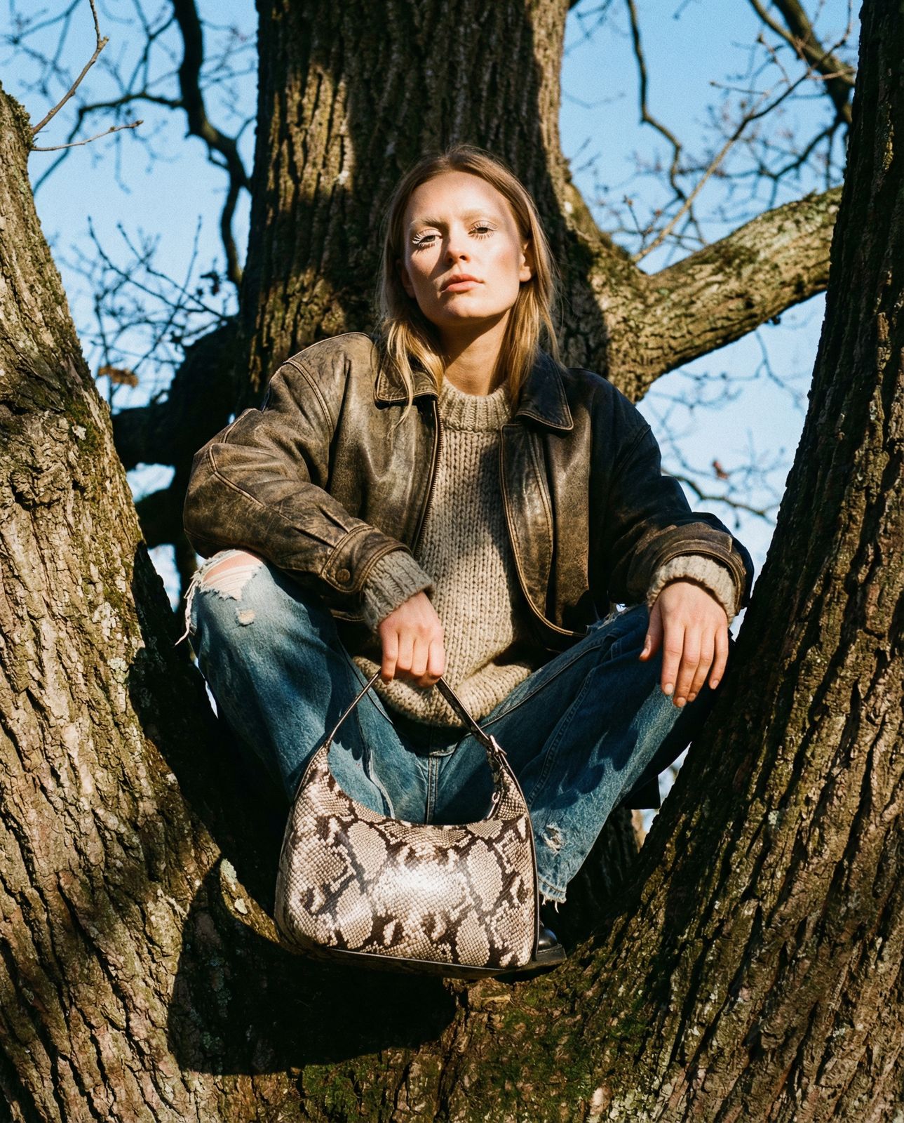 a woman sitting in a tree with a handbag