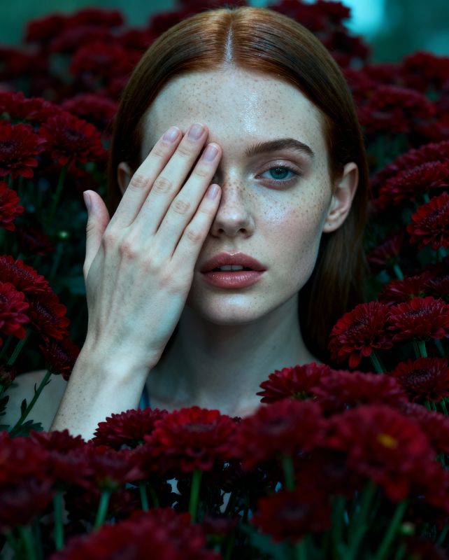 a woman with freckled hair is surrounded by red flowers