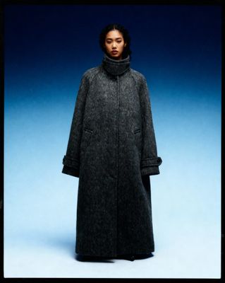 a woman in a long coat standing in front of a blue background