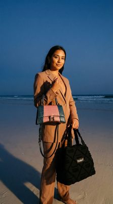 a woman standing on a beach holding a handbag