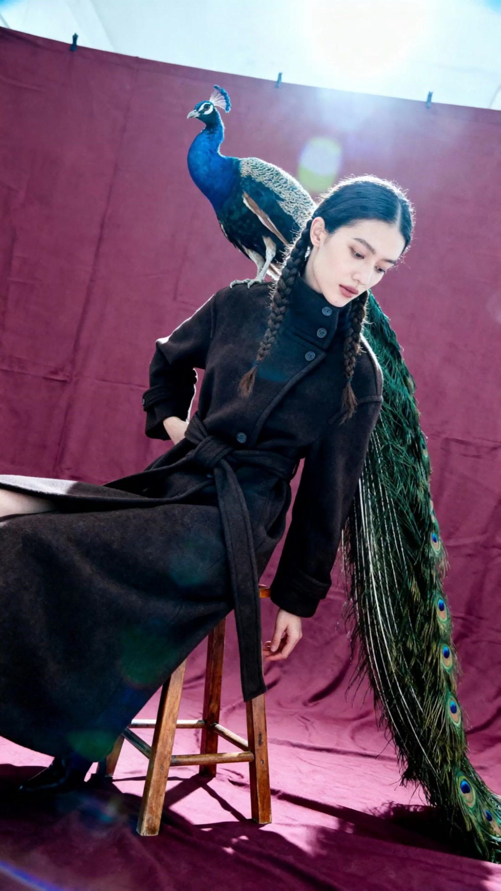 a woman sitting on a stool with a peacock on her head