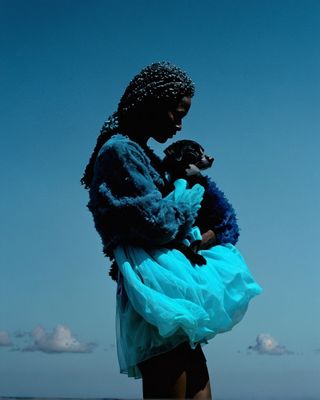 a woman in a blue dress holding a black dog
