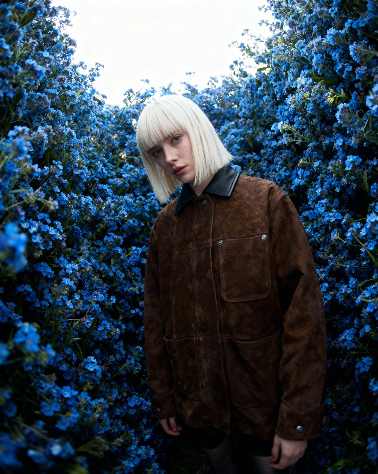 a woman with blonde hair standing in front of blue flowers