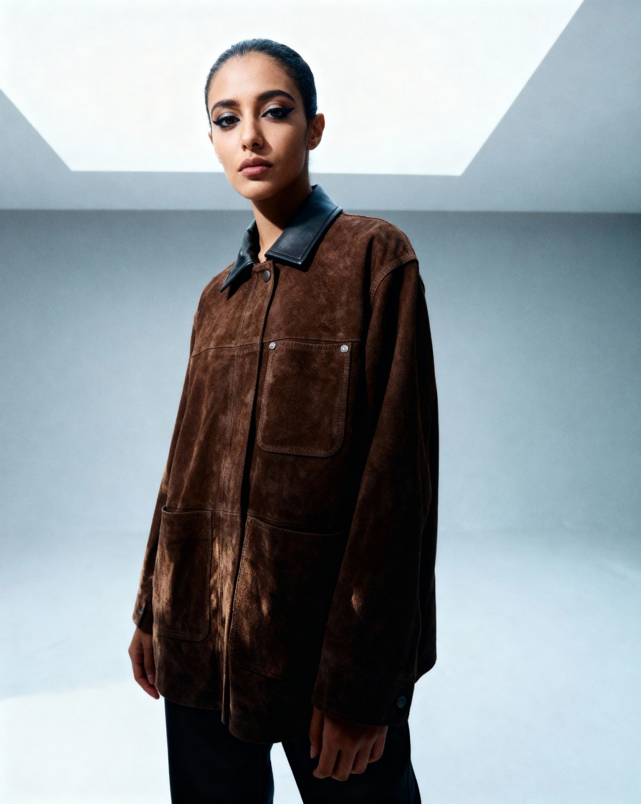 a woman standing in a room wearing a brown jacket