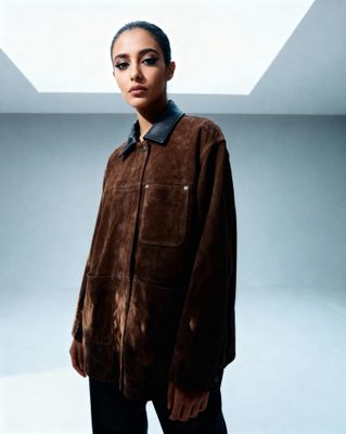 a woman standing in a room wearing a brown jacket