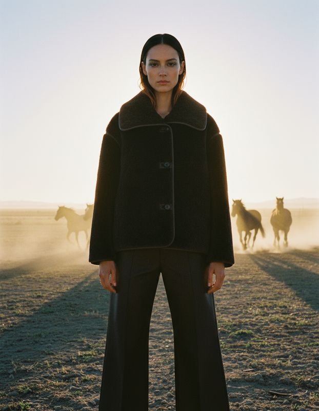 a woman standing in a field with horses in the background