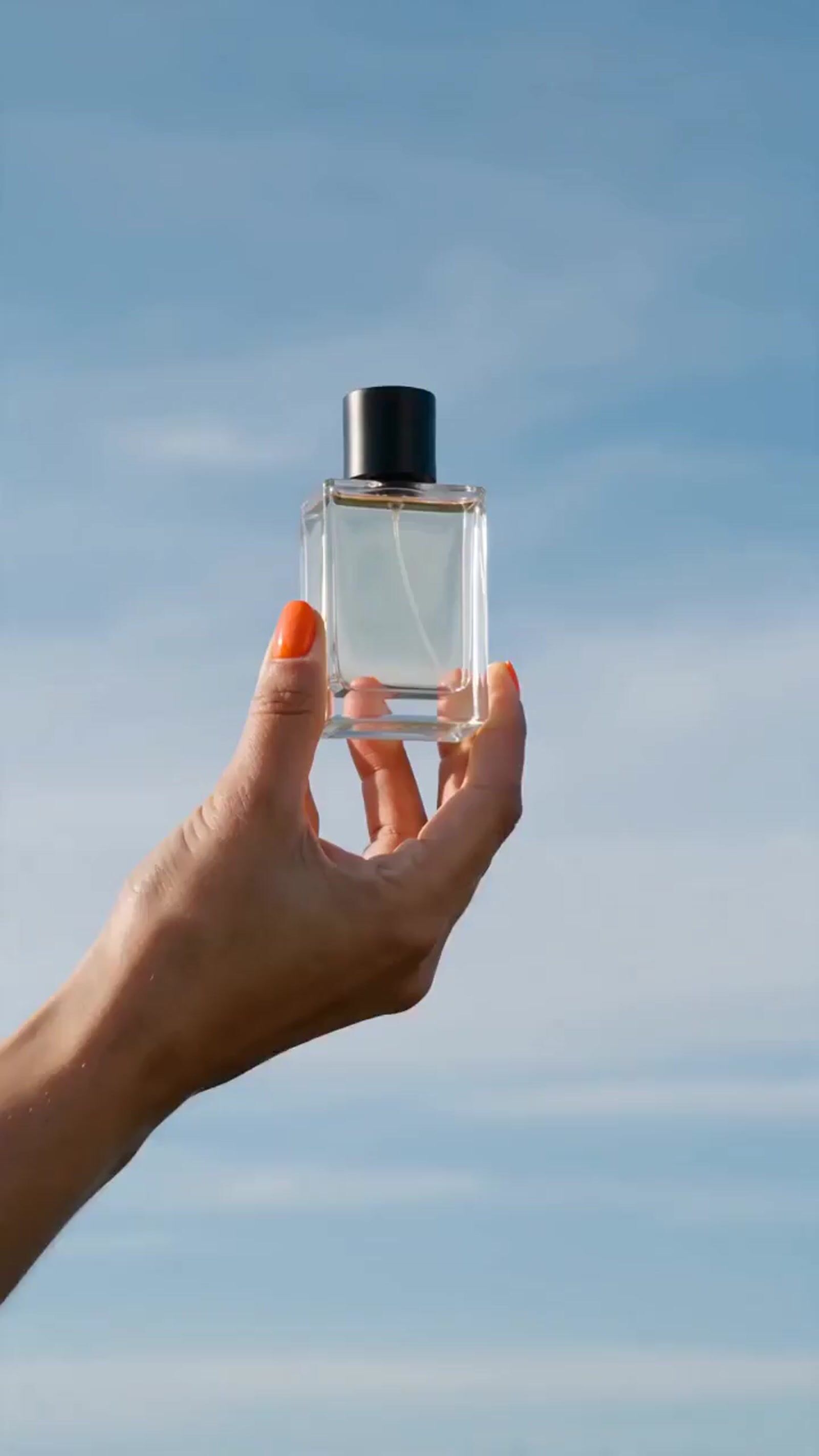 a hand holding a small square bottle of perfume