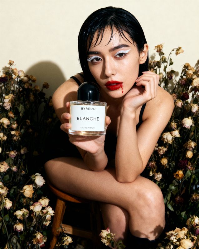 a woman sitting on a chair holding a bottle of perfume