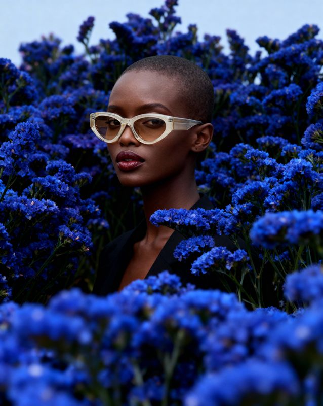 a woman wearing sunglasses standing in a field of blue flowers