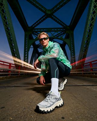 a man in a green jacket crouches on a bridge