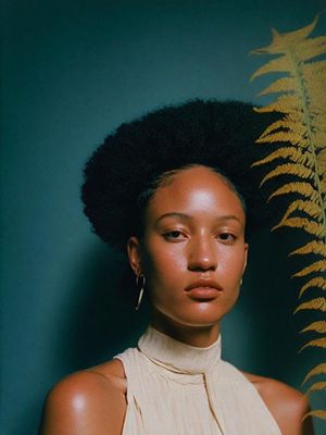 a woman with an afro standing in front of a fern