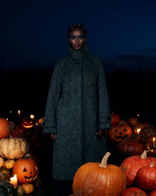 a woman standing in front of a pile of pumpkins