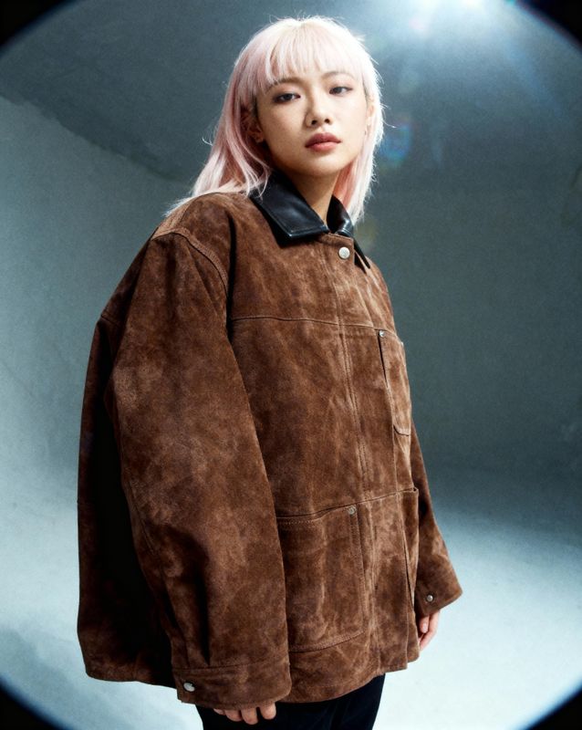 a woman with pink hair wearing a brown jacket