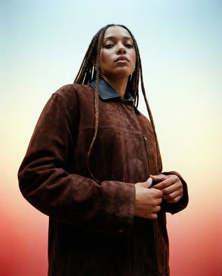 a woman with dreadlocks wearing a brown jacket