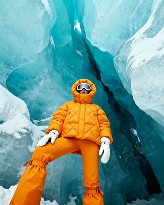 a man in an orange snow suit standing in front of an ice cave