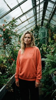 a woman standing in a greenhouse wearing an orange sweatshirt