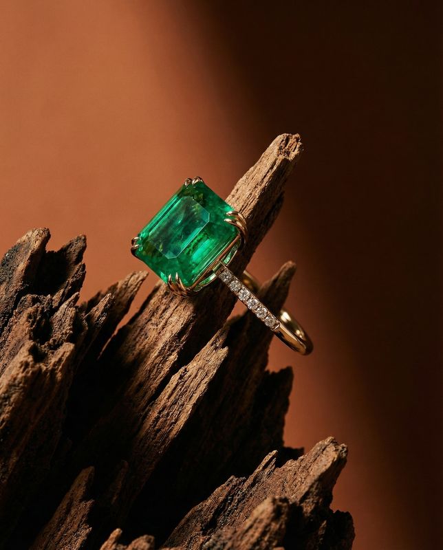 a ring with an emerald and diamond on top of a piece of wood