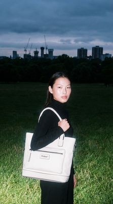a woman standing in a field holding a white bag