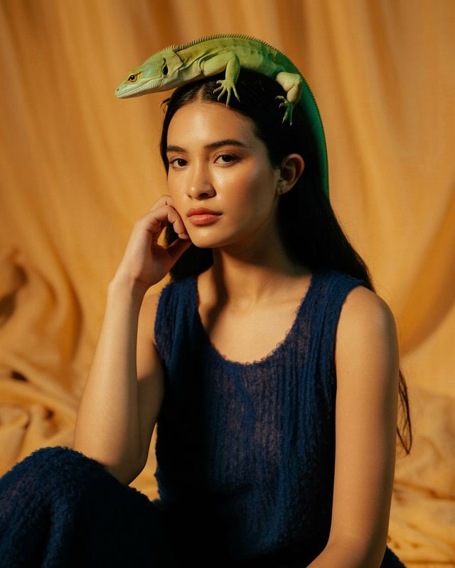 a woman sitting on a bed with a lizard on her head