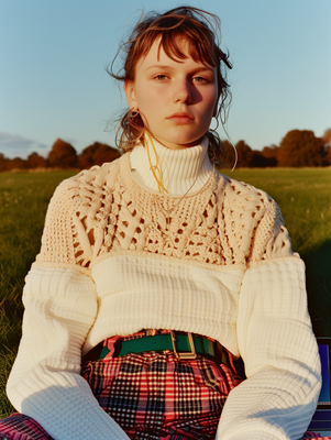 a woman sitting in the grass wearing a sweater