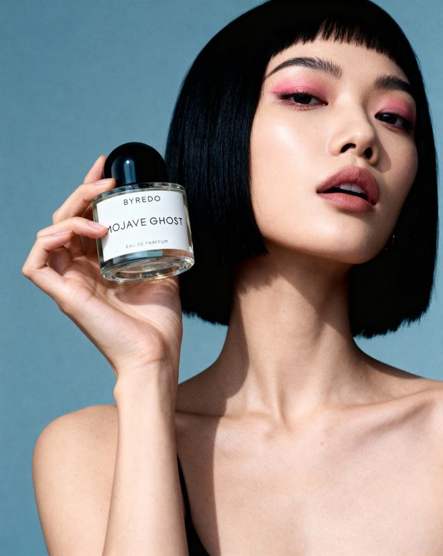 a woman holding a bottle of perfume next to her face