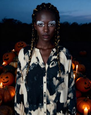 a woman standing in front of a pile of pumpkins