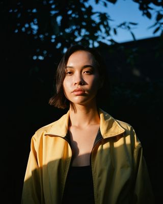 a woman standing in front of a tree wearing a yellow jacket