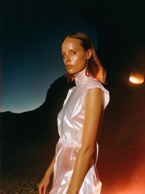 a woman in a white dress standing in front of a fire