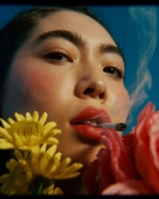 a woman smoking a cigarette next to a flower