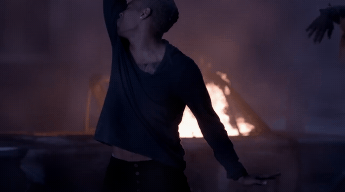 a man standing in front of a fire with his arms in the air