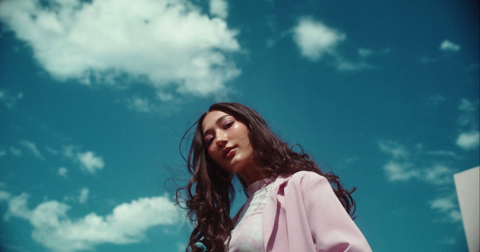 a woman with long hair standing under a cloudy blue sky