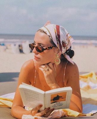 a woman laying on the beach reading a book