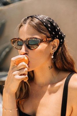 a woman wearing sunglasses and a bandana eating a hot dog