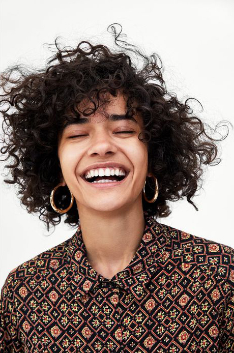 a woman with curly hair smiling and wearing earrings