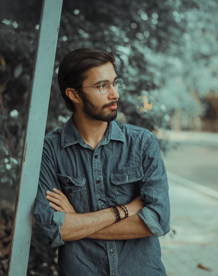 a man with glasses leaning against a pole