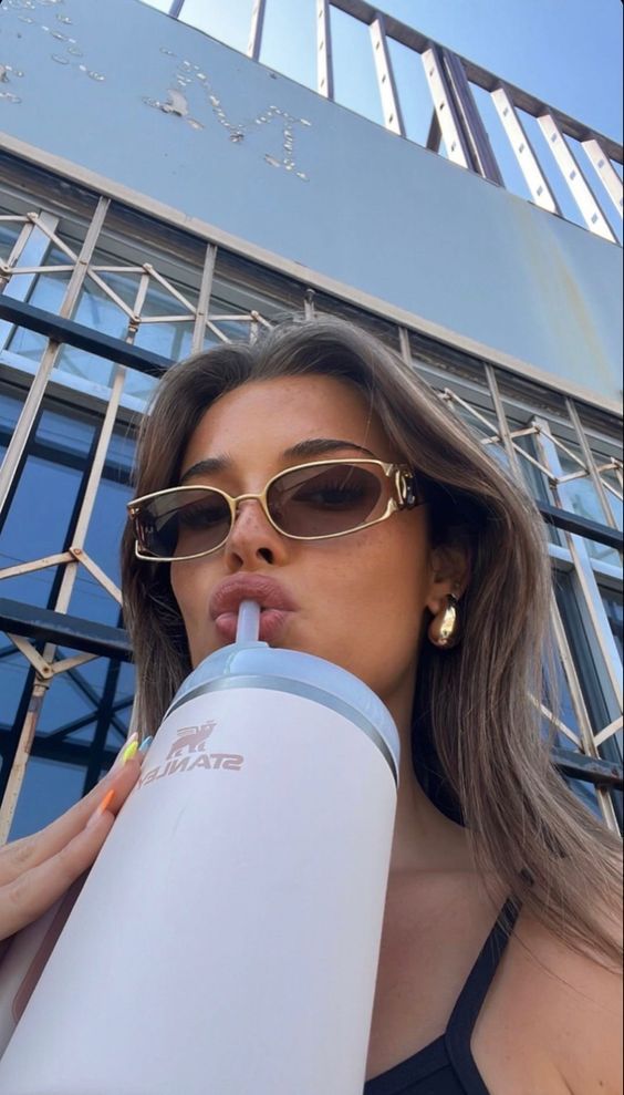 a woman wearing sunglasses drinking from a water bottle