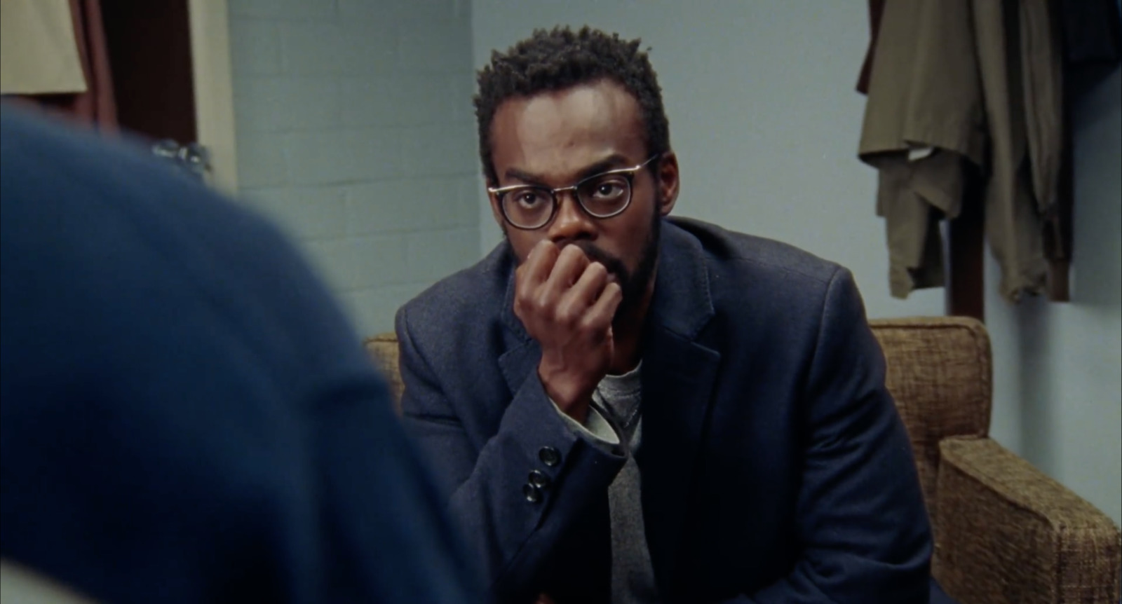 a man in a suit and glasses sitting in front of a mirror