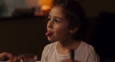 a little girl sticking out her tongue while sitting at a table